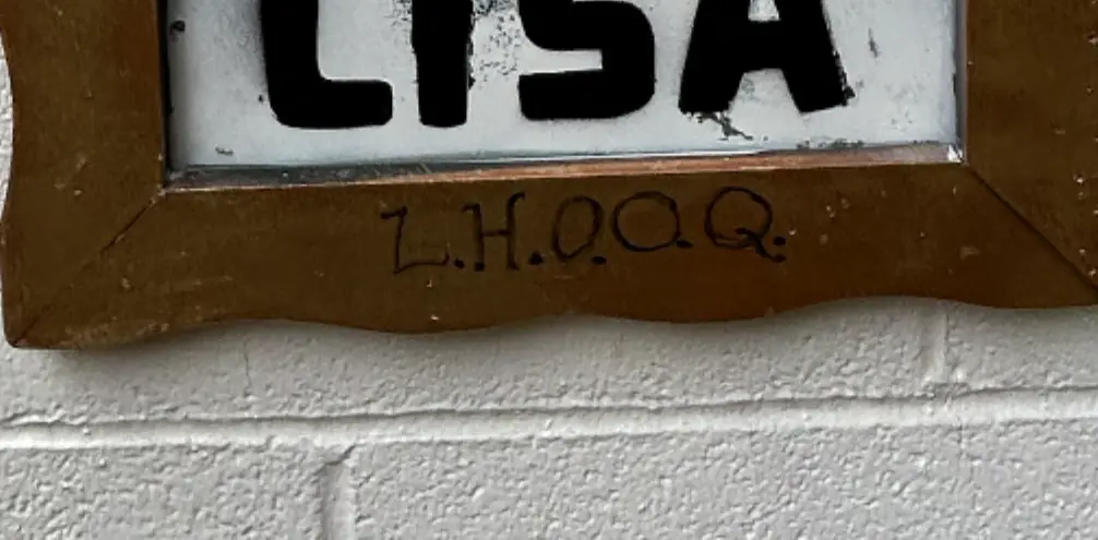 Close-up of the bottom rail of a gold frame, with L.H.O.O.Q. hand-lettered in black marker under the stenciled word LISA